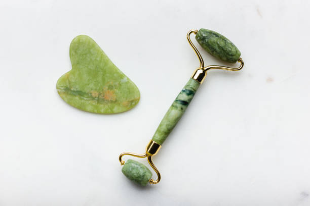 Green jade roller and gua sha tool on a white background